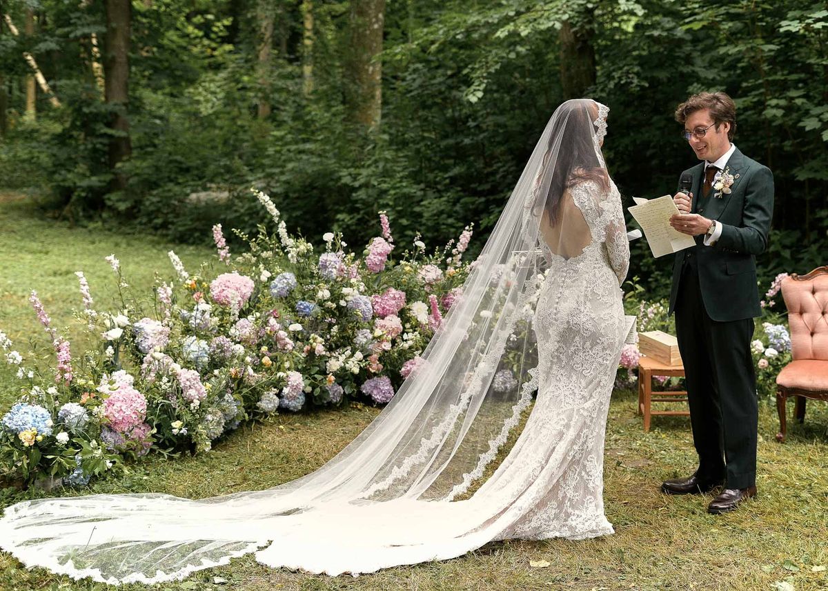 Groom reading vows to bride during outdoor woodland ceremony with floral backdrop