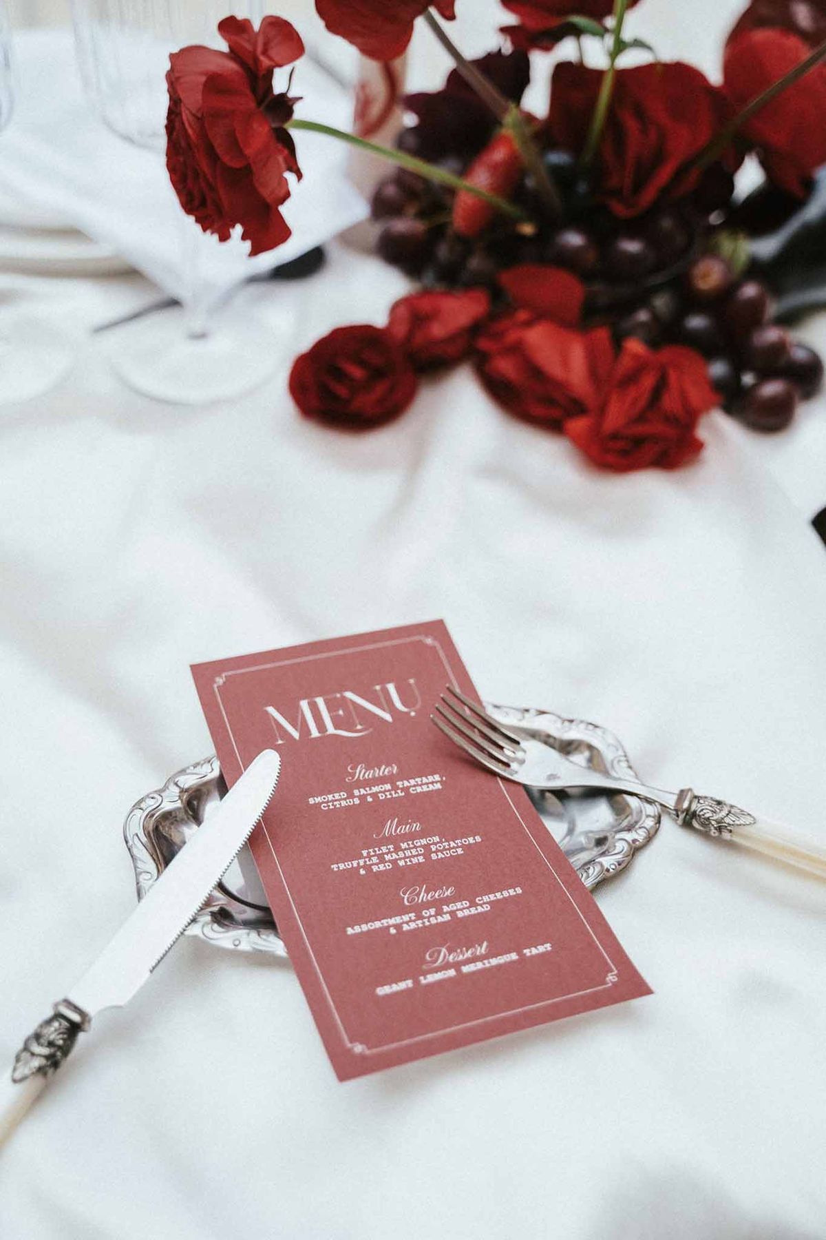 Formal table setting with dusty rose menu card and burgundy florals on silver charger plate