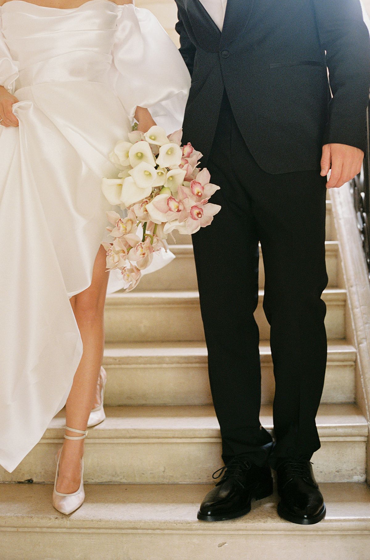 Bride and groom standing together on stone staircase showing wedding attire and bridal bouquet