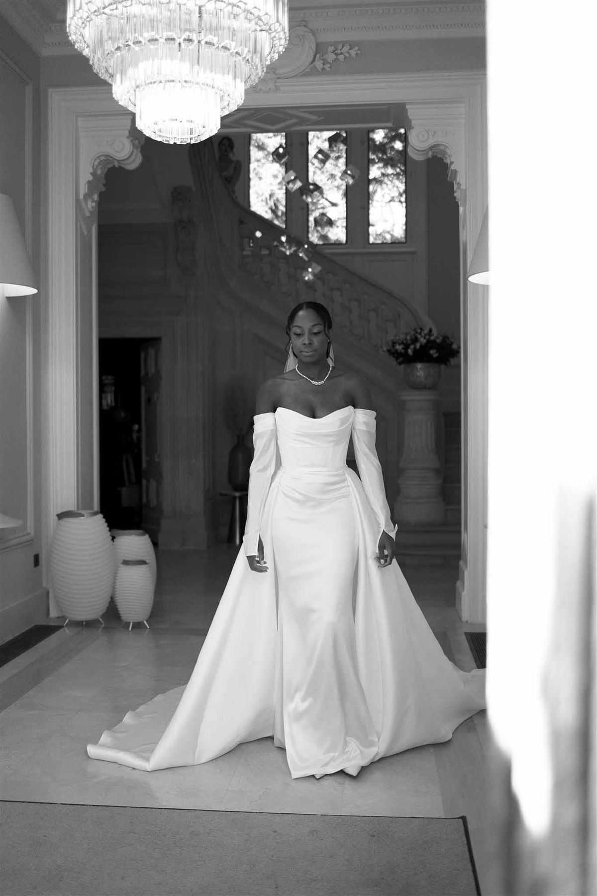 Bride in wedding gown standing in elegant neoclassical interior hallway with crystal chandelier