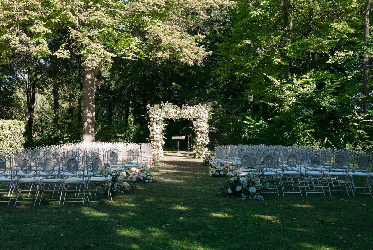 Outdoor wedding ceremony setup with floral arch in wooded garden venue