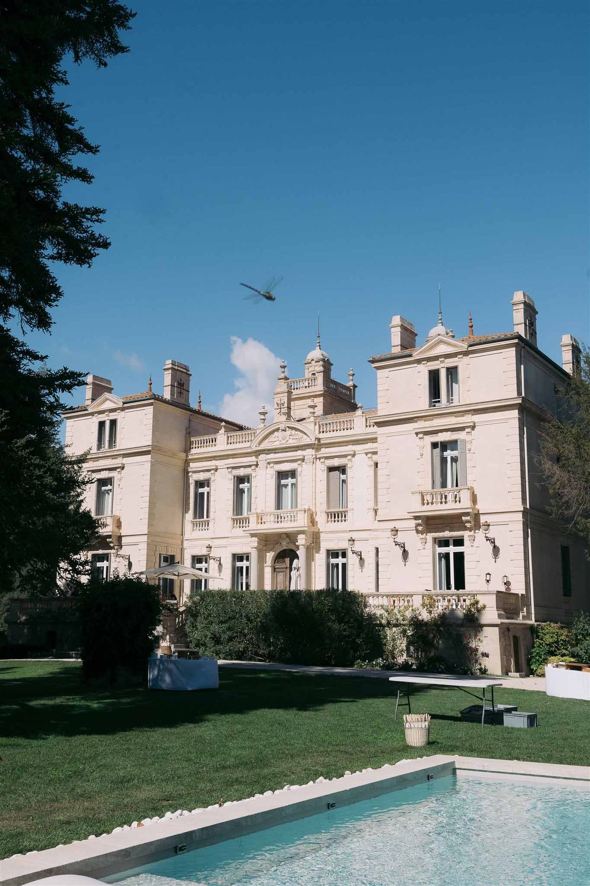 Wide view of neoclassical mansion with pool and reception setup on manicured grounds