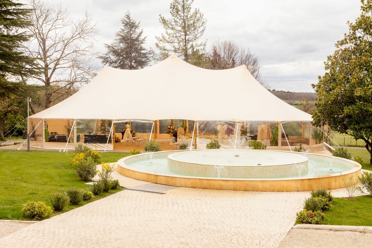 Stretch tent reception setup on stone terrace with fountain in foreground at a French country estate