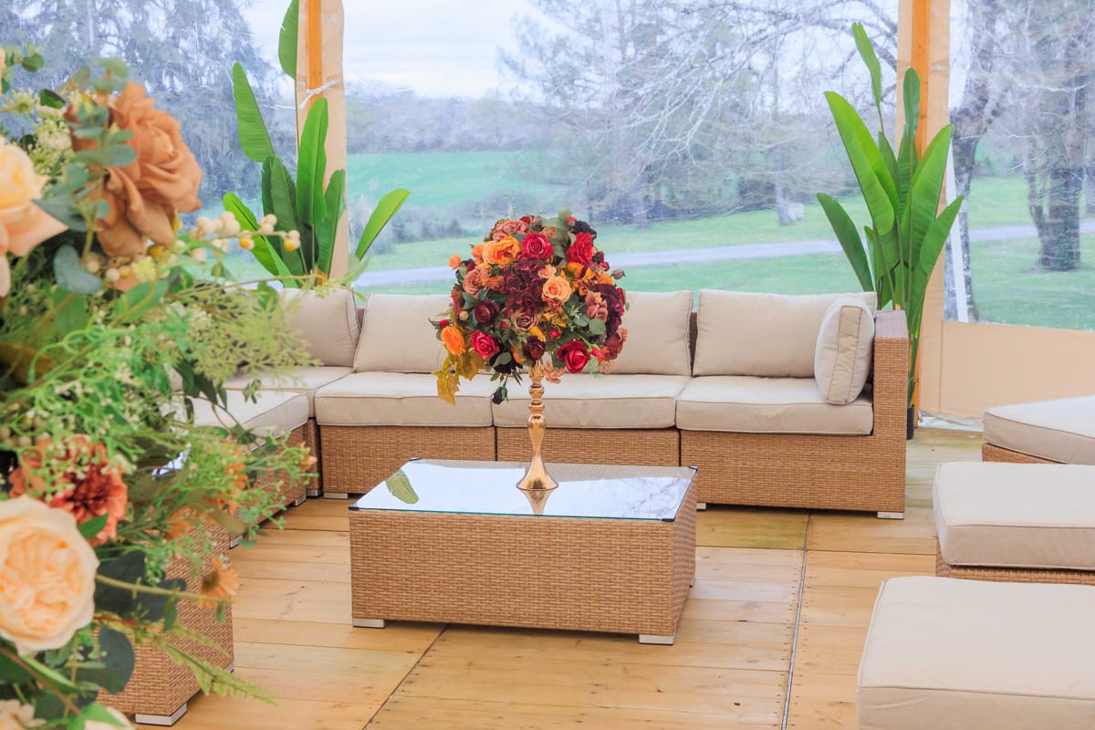 Marquee lounge area with wicker sofa and autumn floral arrangements in burgundy, orange, and peach tones