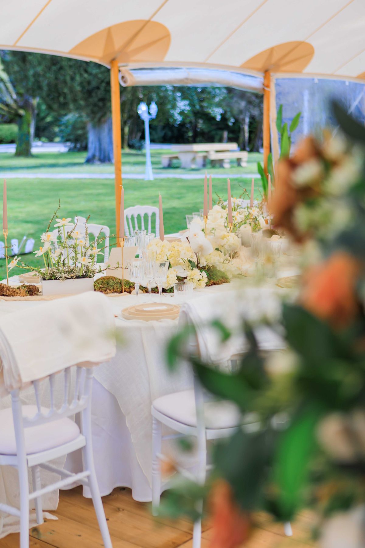 Long sailcloth marquee table with cream hydrangea runner and blush taper candles on white Chiavari chairs in garden