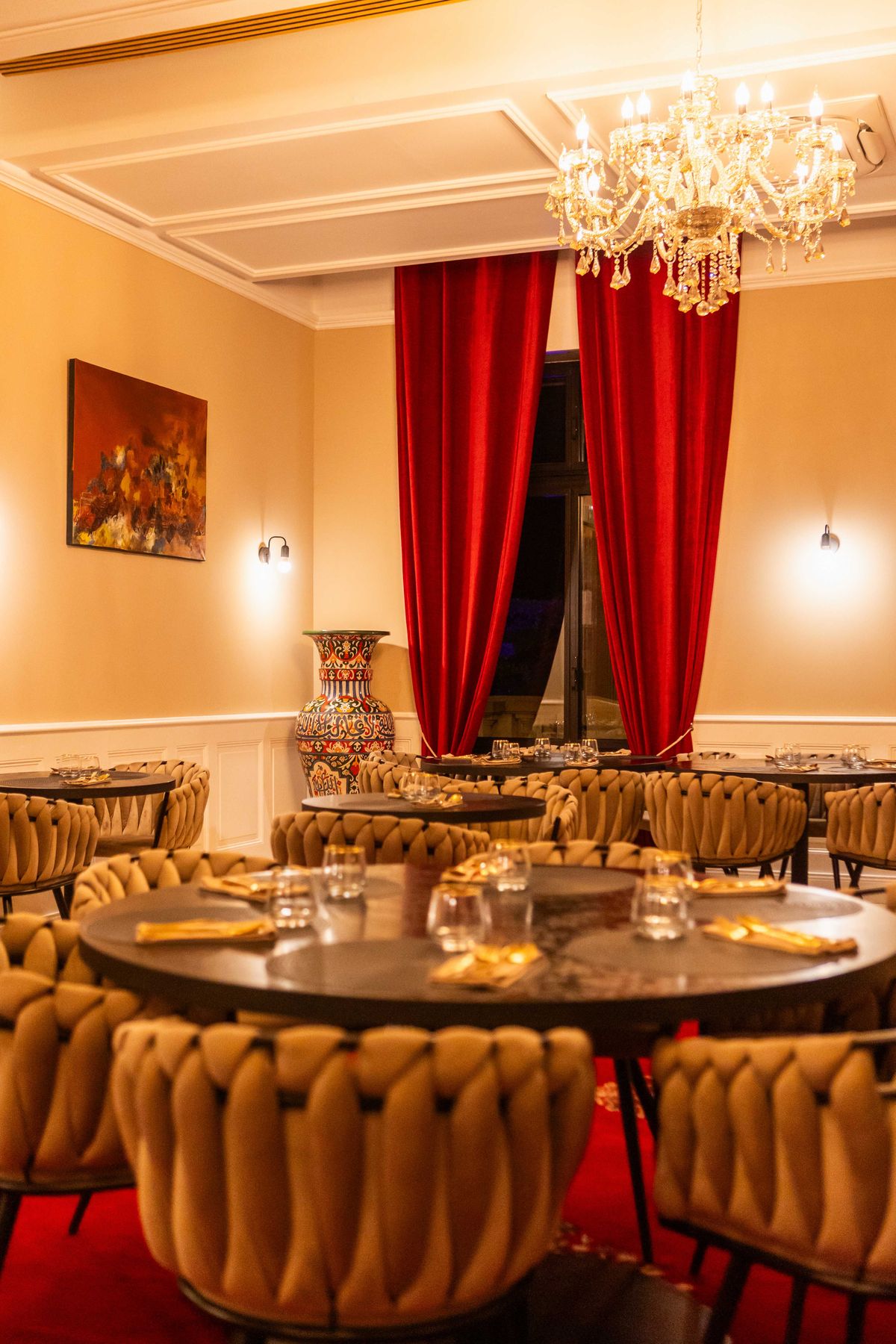 Formal dining room with red velvet curtains, crystal chandelier, braided camel chairs, and oil painting