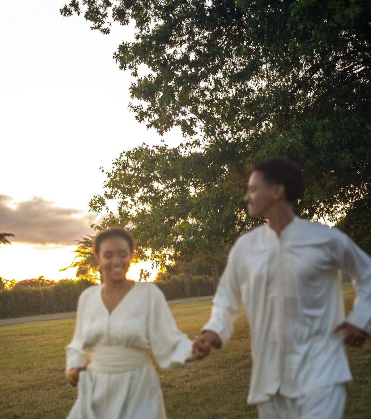 Bride and groom running hand-in-hand across lawn at golden hour, motion-blurred candid shot