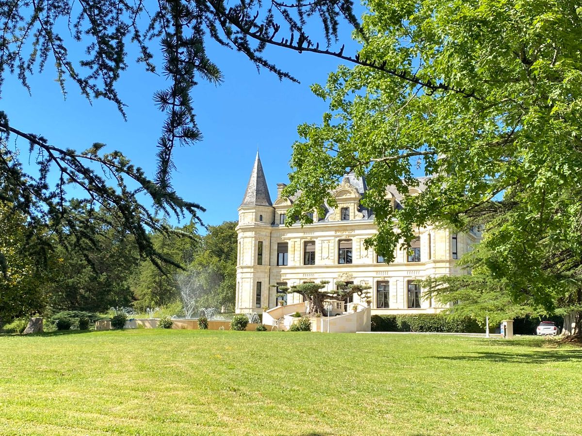 19th-century chateau with cream stone facades, slate turret, fountain, and ornamental tree at entrance