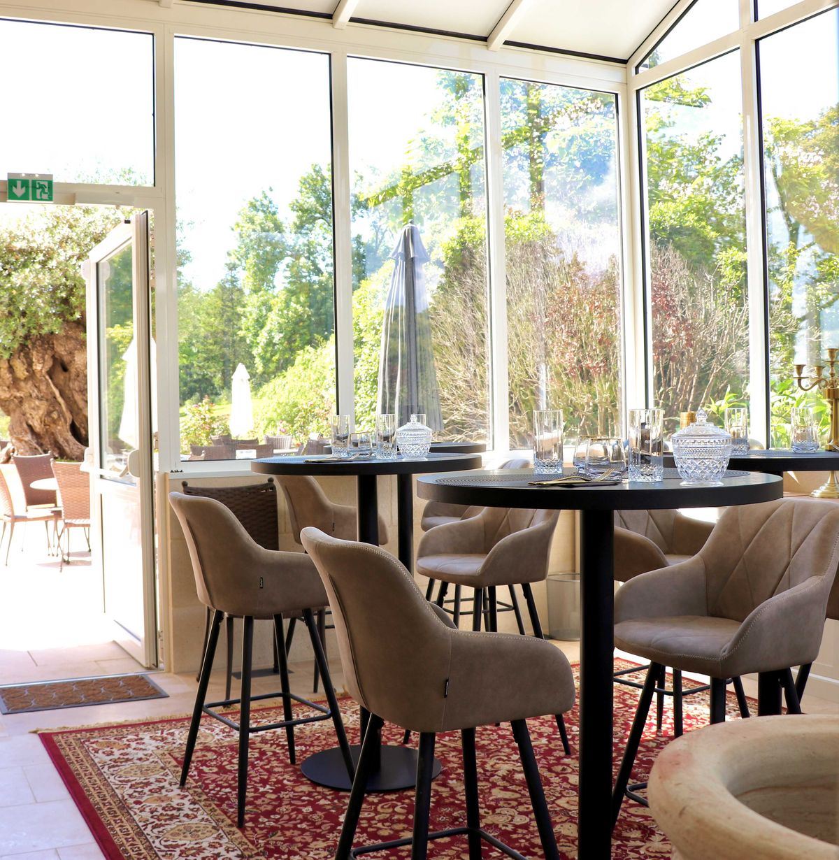 Glass conservatory cocktail space with high-top tables crystal glassware and garden view