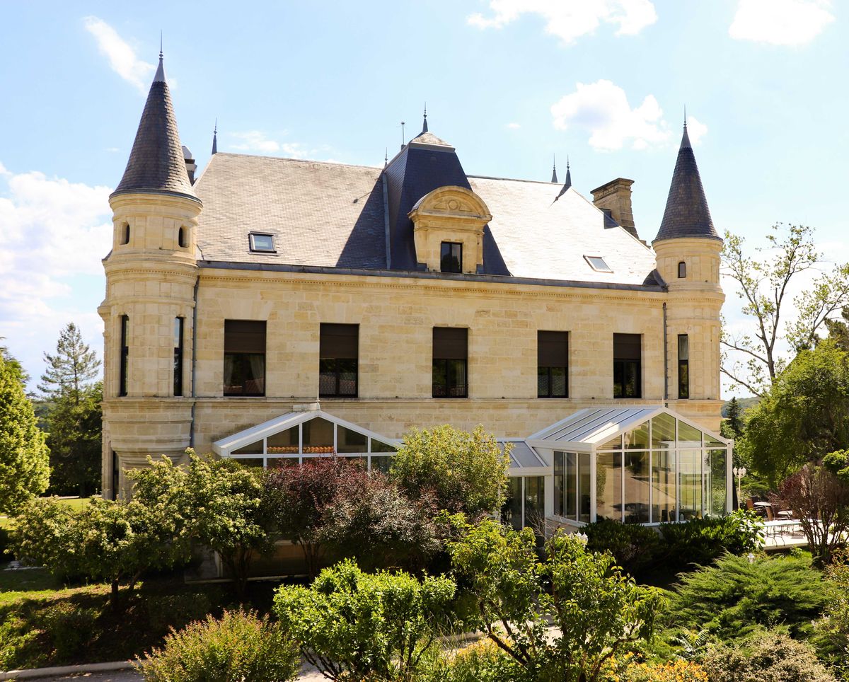 Limestone chateau with four corner turrets, slate mansard roof, and modern glass conservatory extension