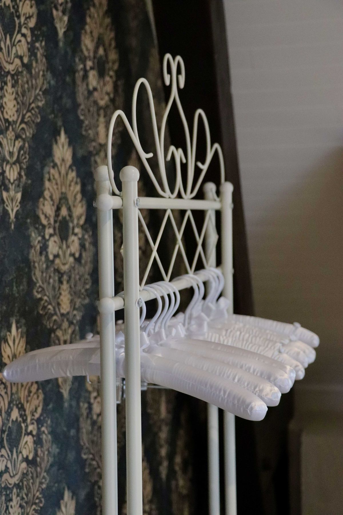 White wrought-iron garment stand with satin-padded hangers against navy damask wallcovering