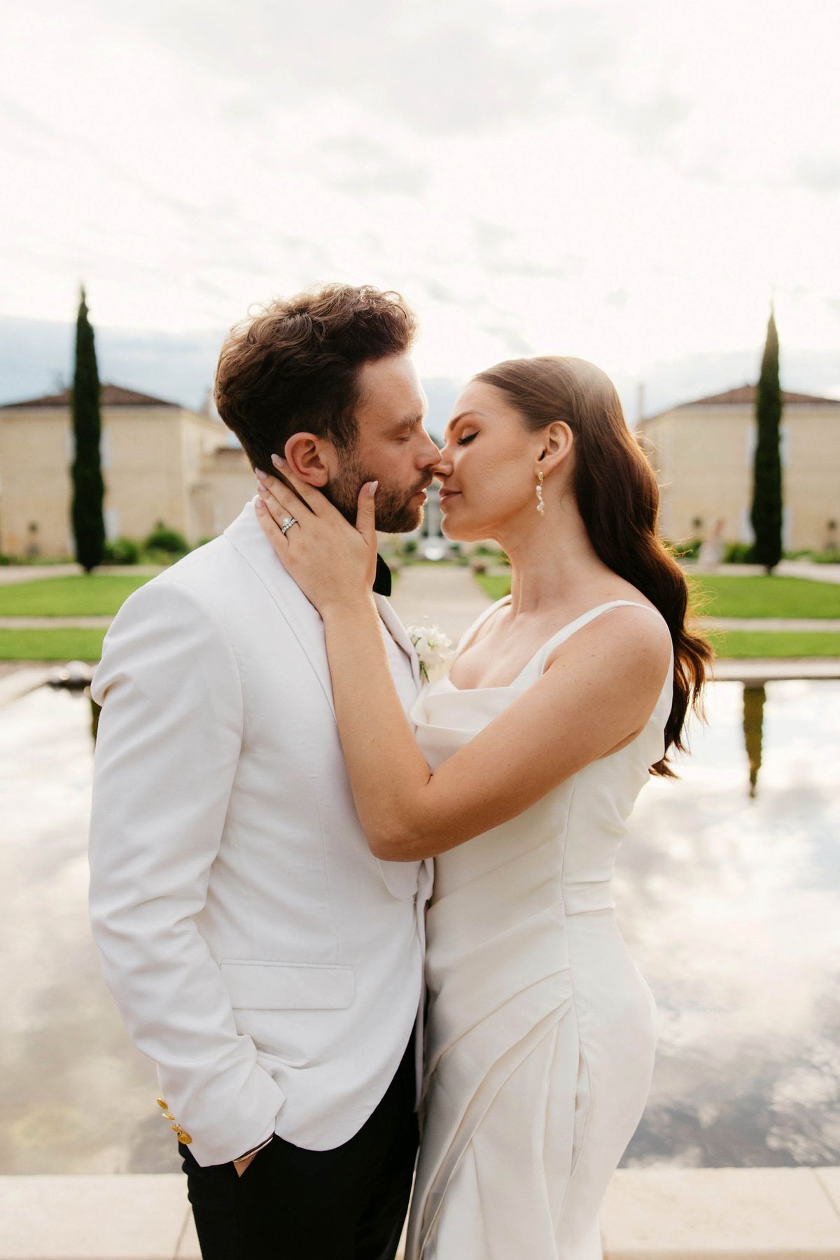 Couple kissing by water feature at European-style wedding venue with stone architecture