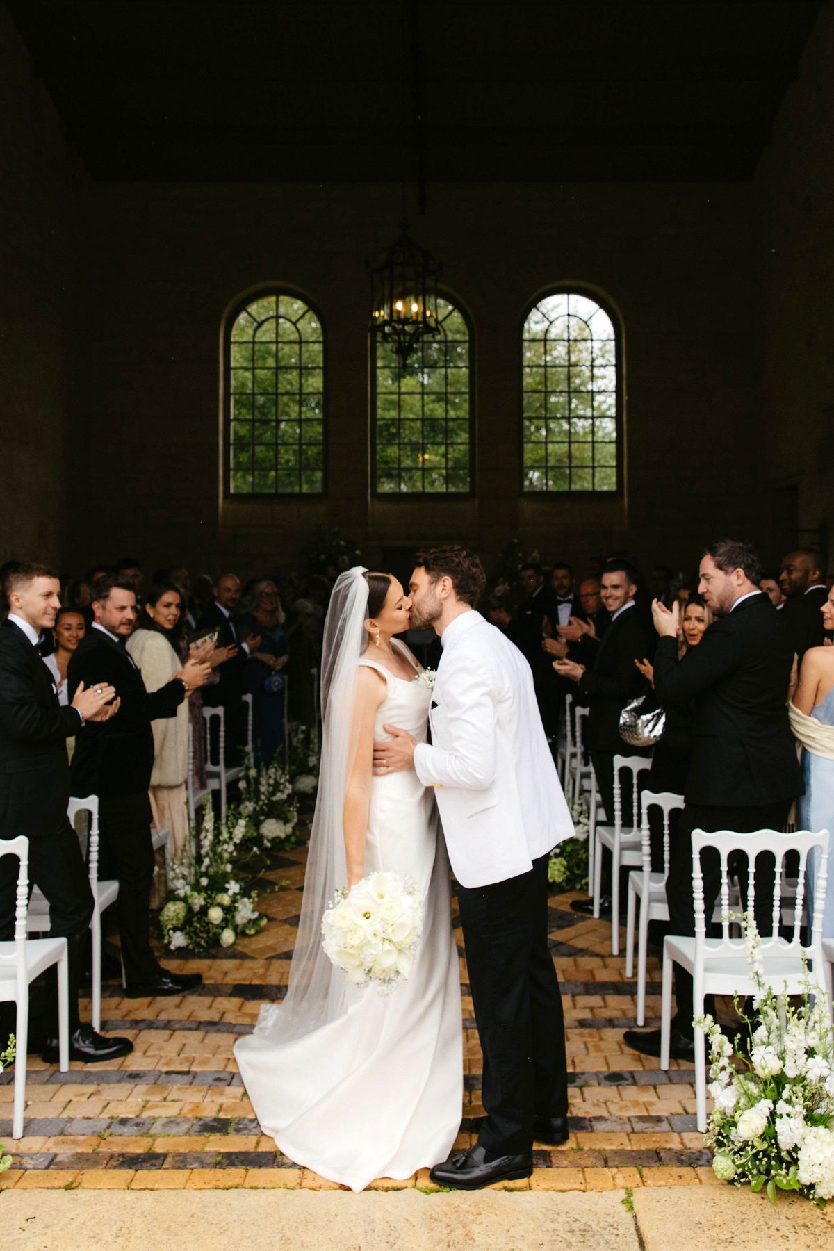 Bride and groom first kiss during ceremony recessional in indoor chapel with guests applauding