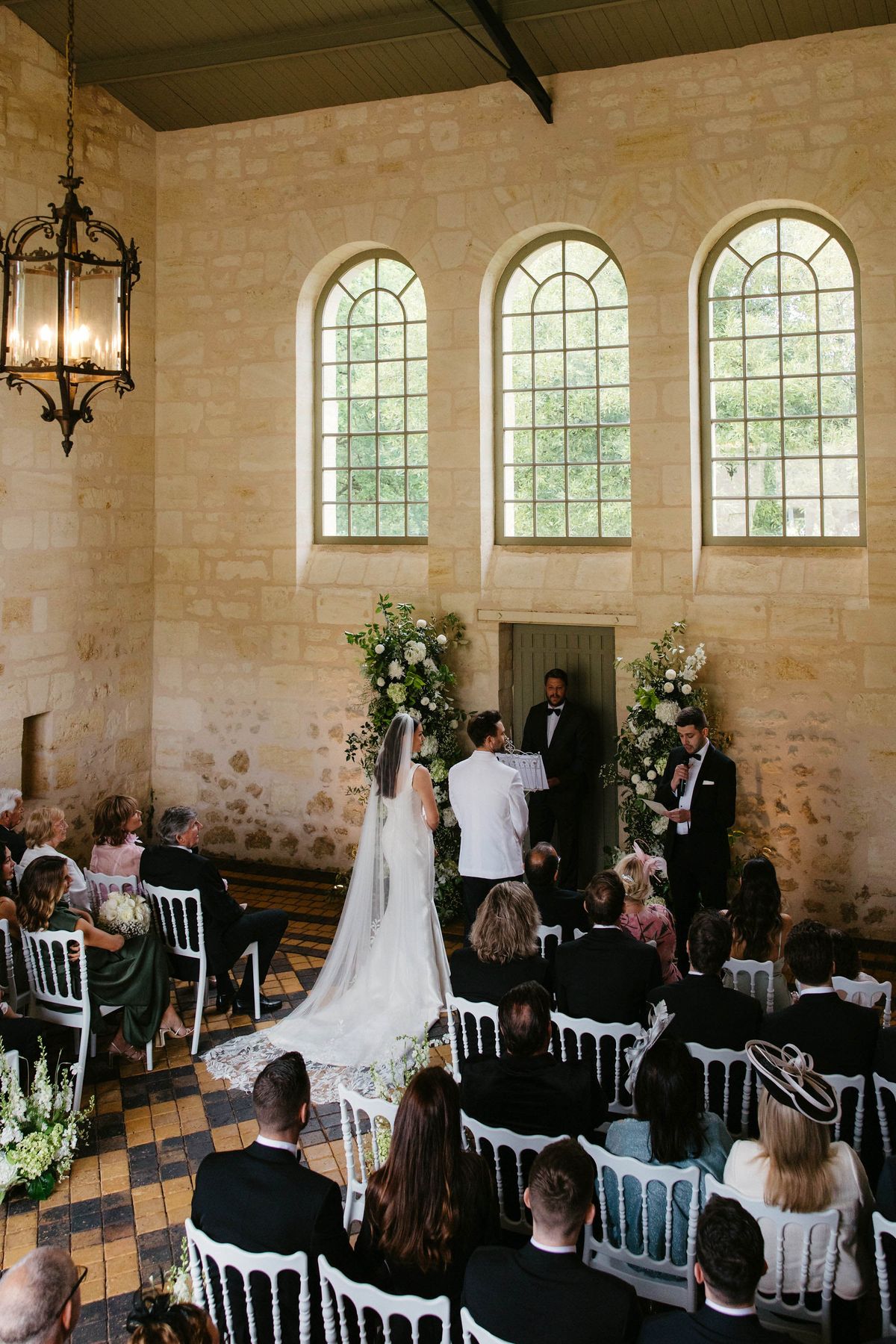 Wedding ceremony in historic stone chapel with guests in white Chiavari chairs
