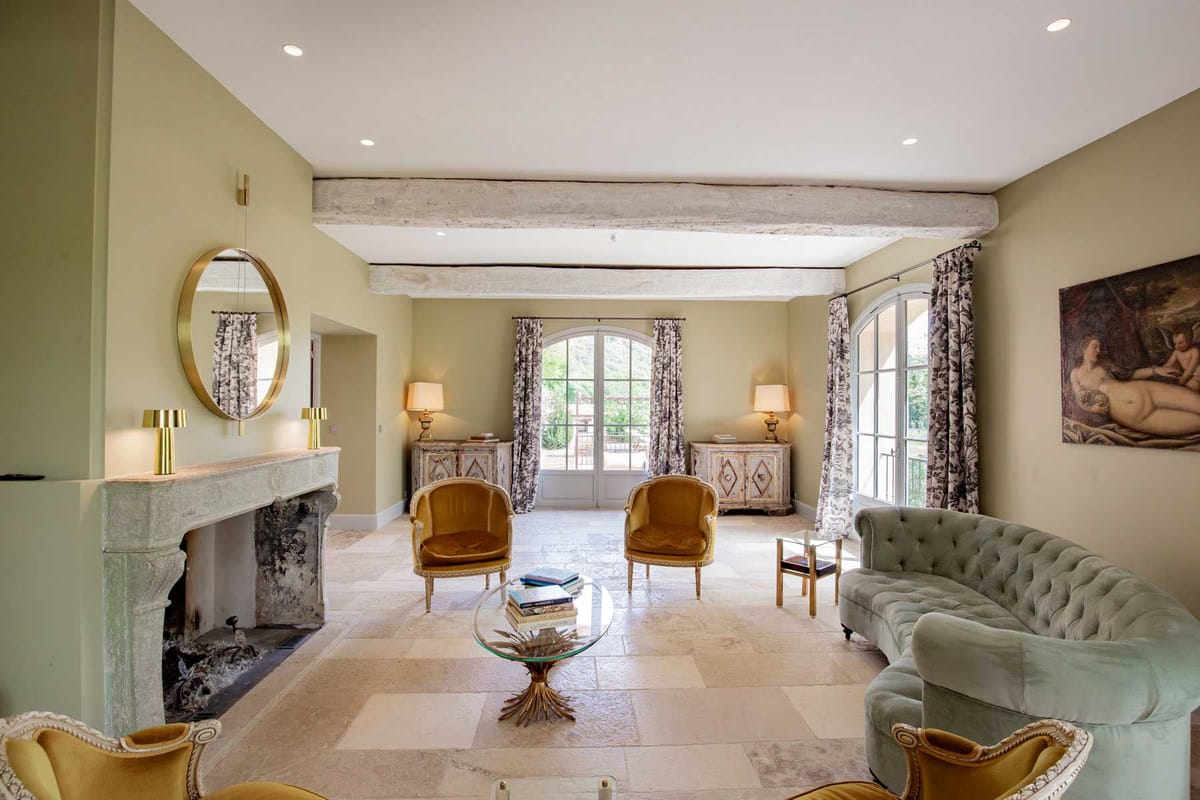 Sage-green sitting room with Chesterfield sofa, gold velvet armchairs, stone fireplace, and arched doors