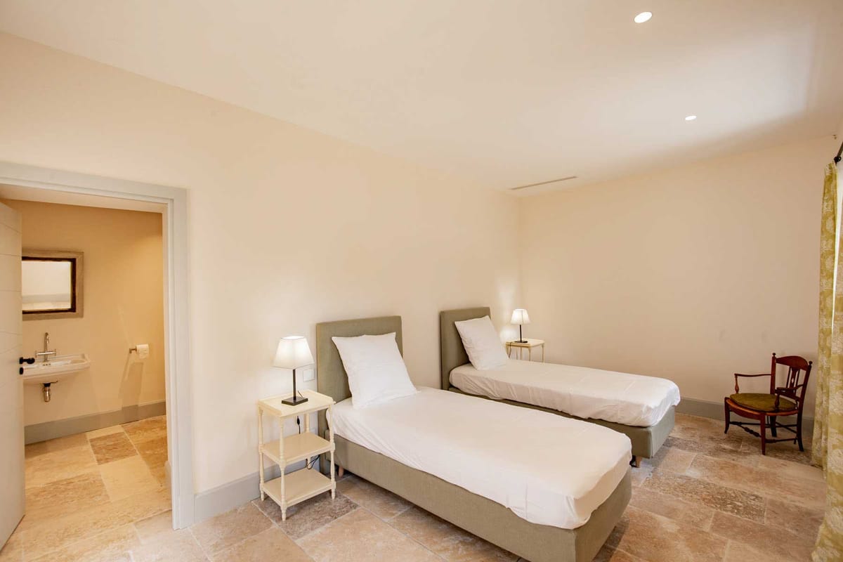 Guest bedroom with sage green headboards, white linens, and en-suite bathroom