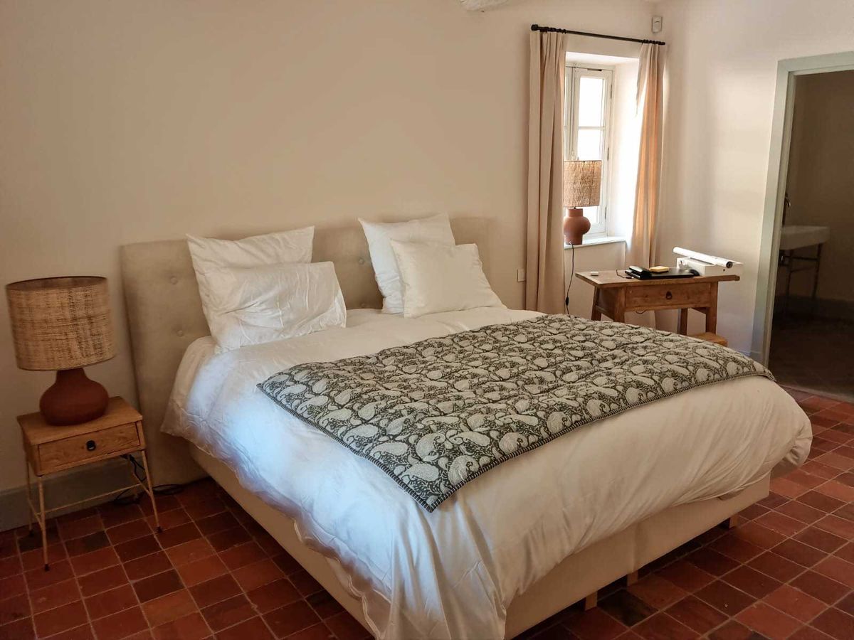 Guest bedroom with linen headboard, terracotta tiles, rattan lamps, and green block-print throw