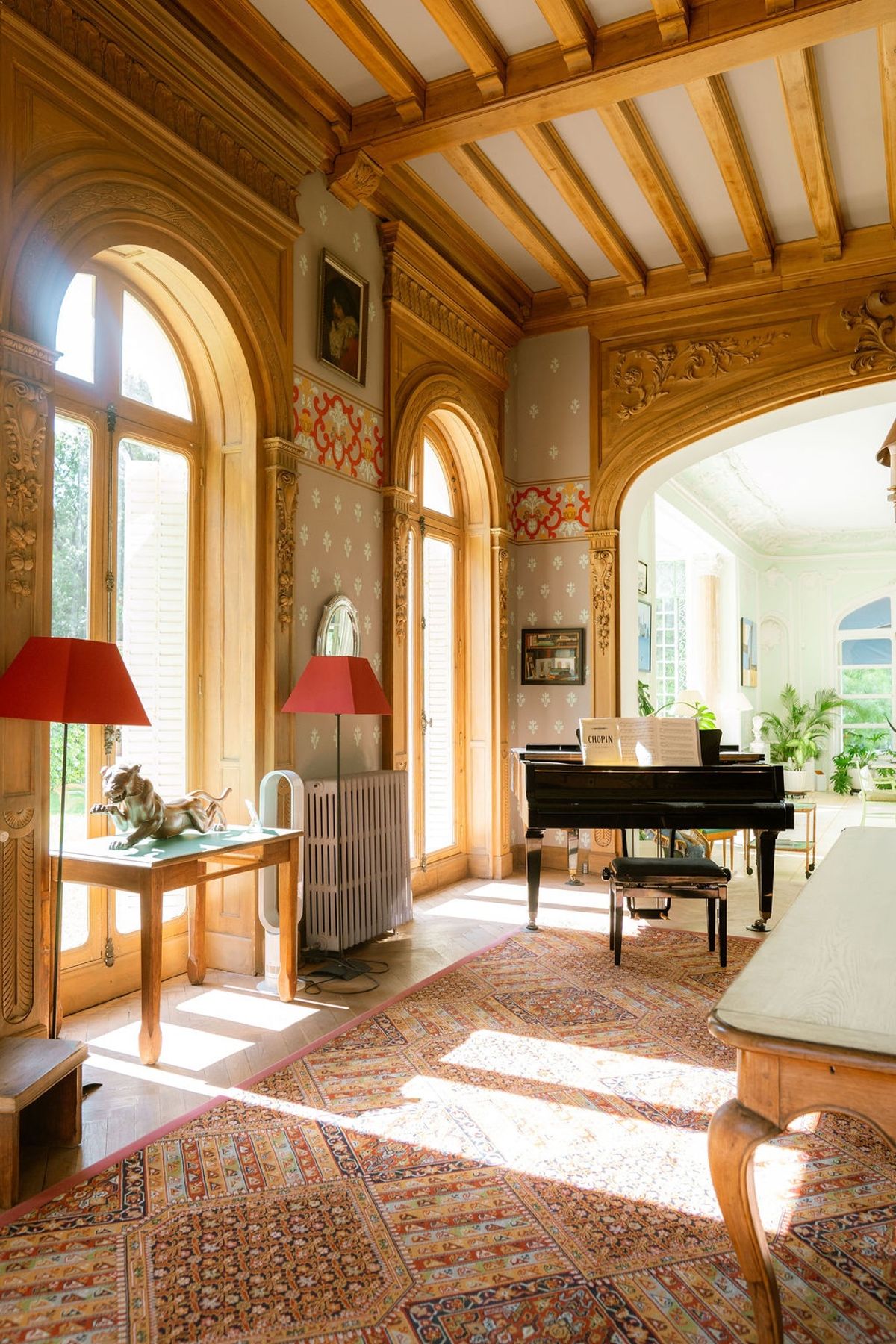 Sunlit piano room with red lamps and timber archway at Domaine Rocabella, French Riviera