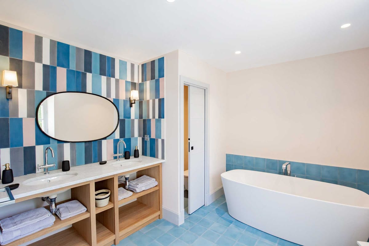 Modern bathroom with patchwork blue and pink tile wall, freestanding white bathtub, and oak vanity