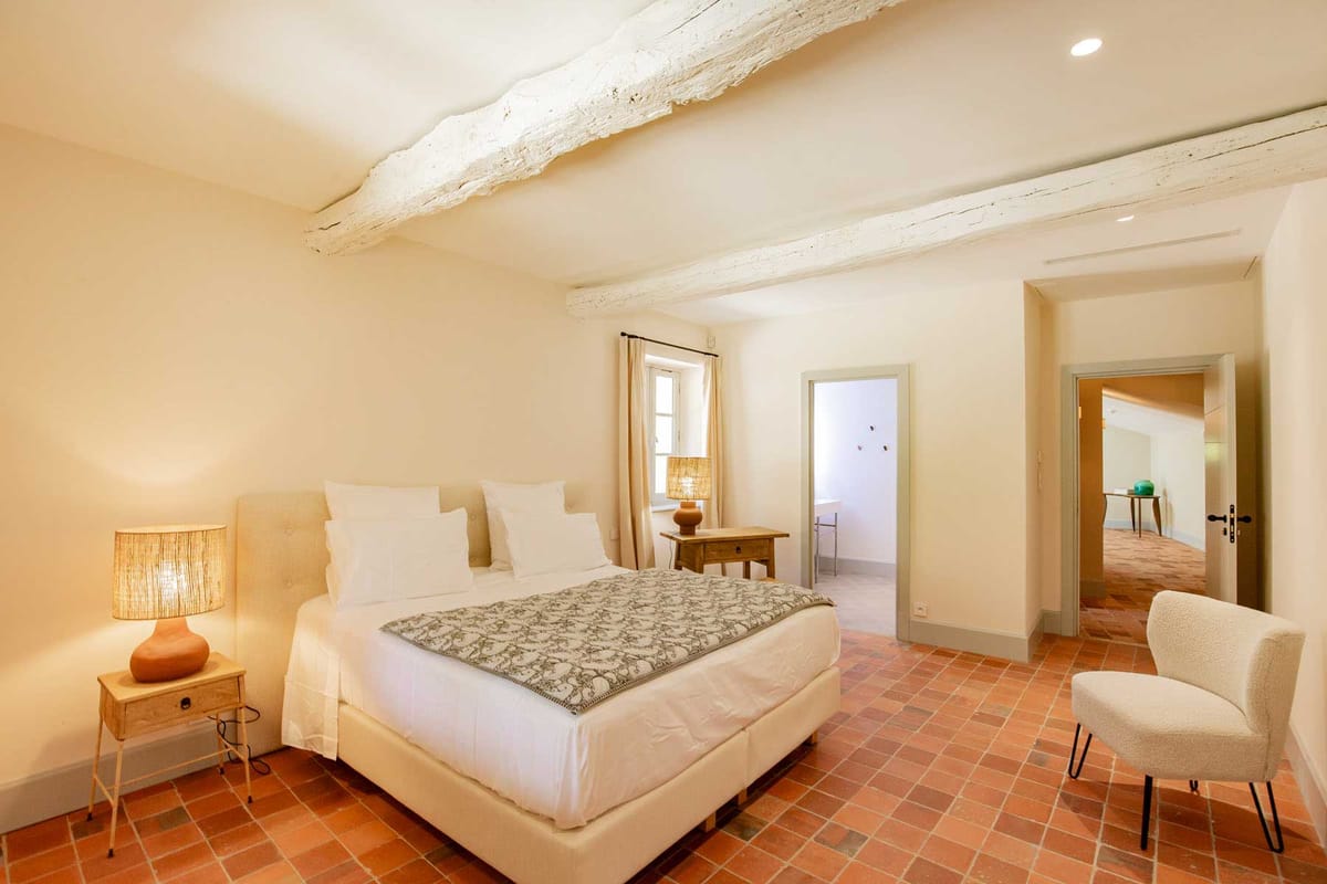 Rustic-modern guest room with terracotta tiles, whitewashed beams, linen headboard, and rattan lamp