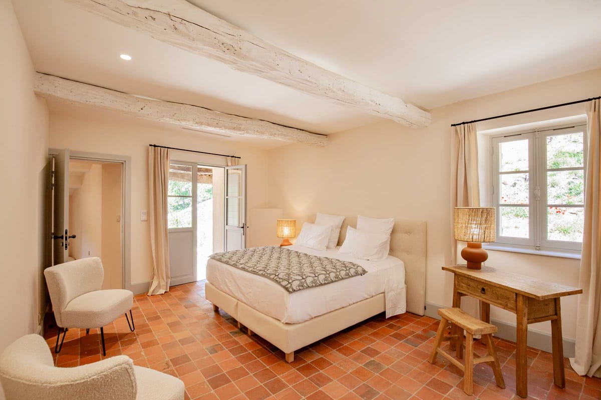 Provencal bedroom with terracotta floors exposed beams cream upholstered bed and rattan lamps