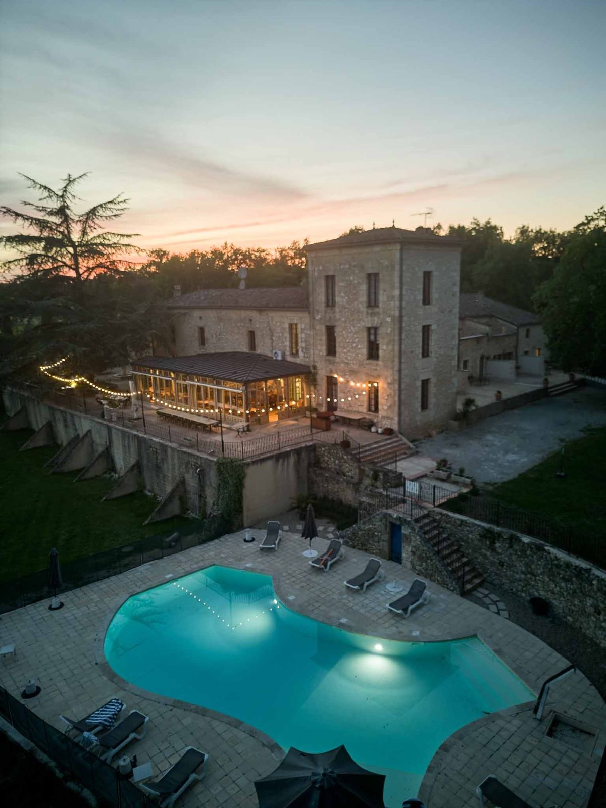 Dusk aerial of illuminated pool and chateau with string lights at Chateau de Sanse