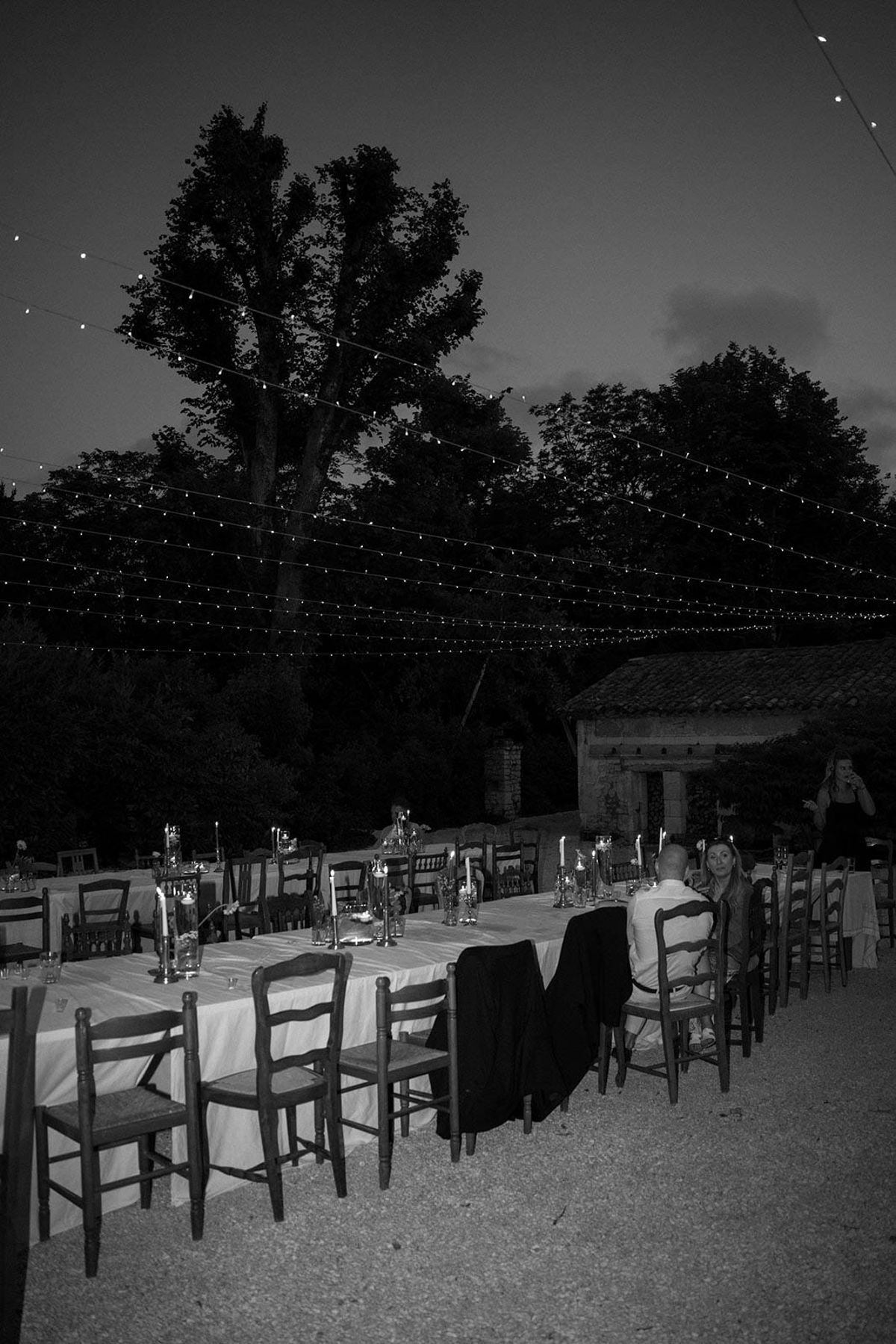 Black and white outdoor reception dinner setup with string lights in rustic courtyard