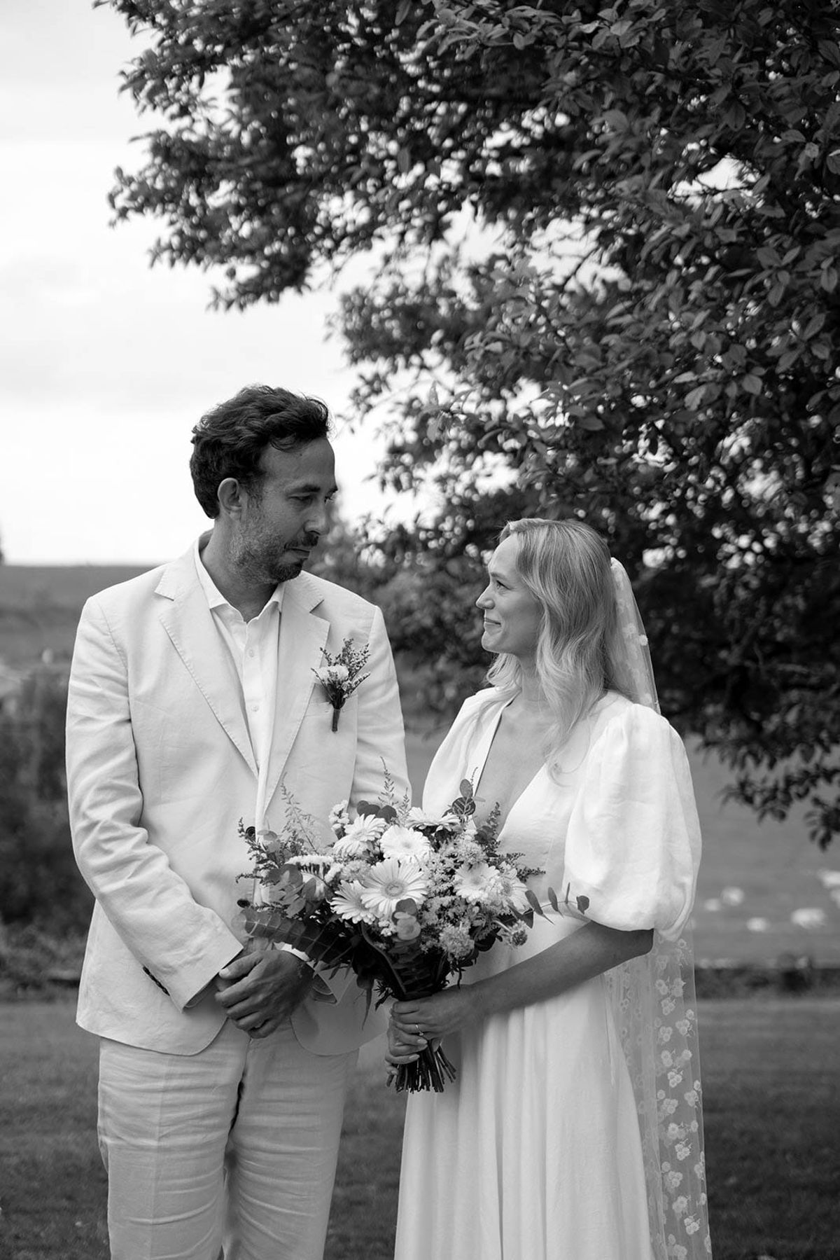 Bride and groom portrait under flowering tree branches in outdoor garden setting