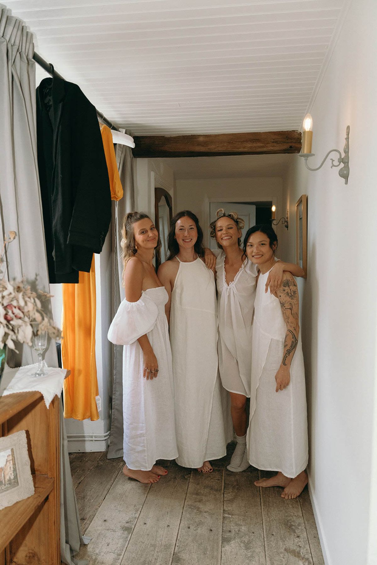 Four bridesmaids in linen robes during getting ready preparations in rustic hallway with exposed beams