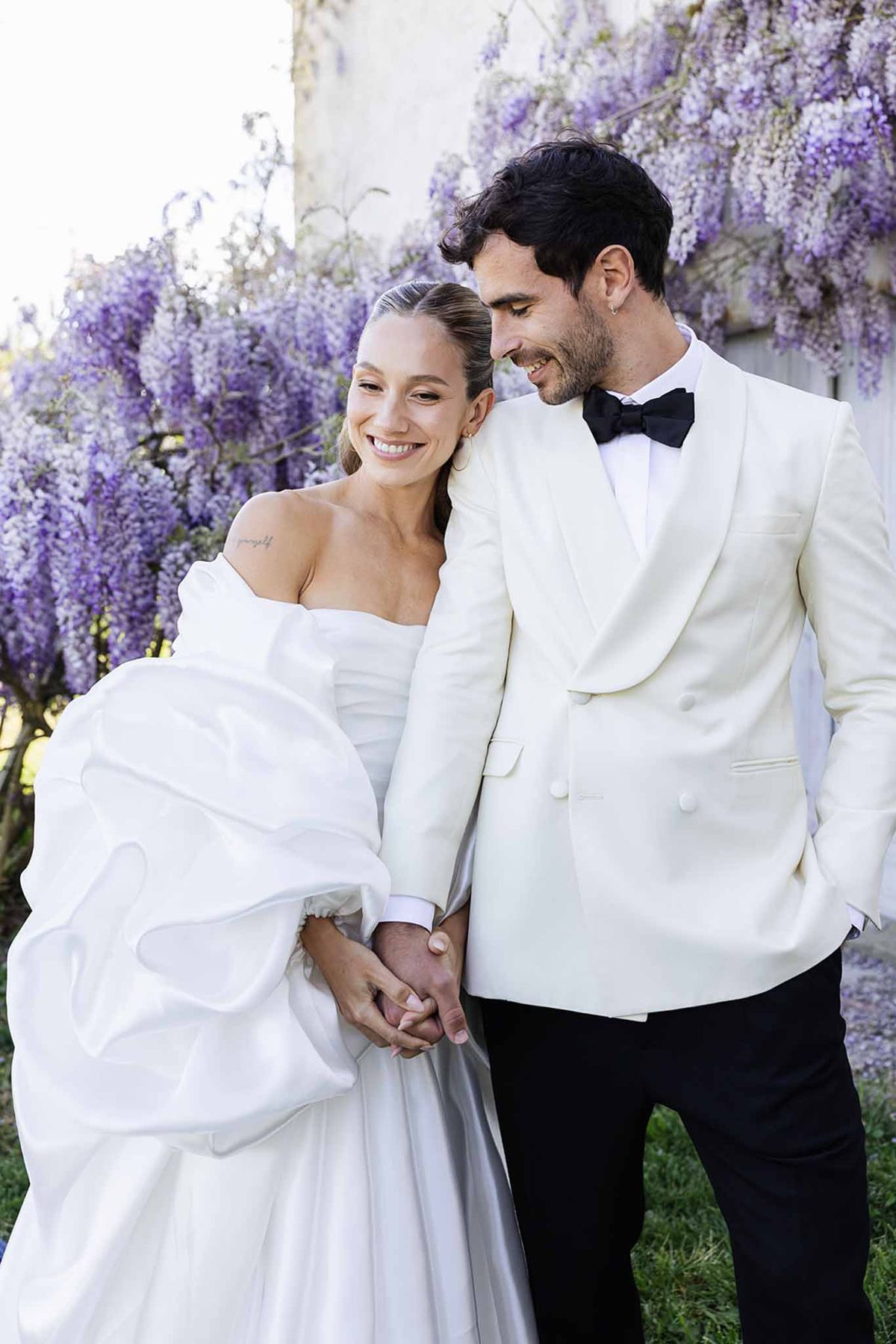 Bride and groom intimate portrait surrounded by purple wisteria blooms in garden setting