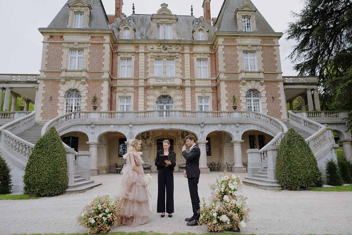 Bride in blush pink tulle gown and groom during ceremony on gravel forecourt of Belle Epoque chateau