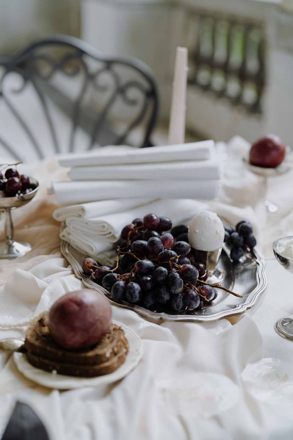 Close-up of ivory and silver wedding tablescape with antique silver trays, dark grapes, pomegranates, and white taper candles