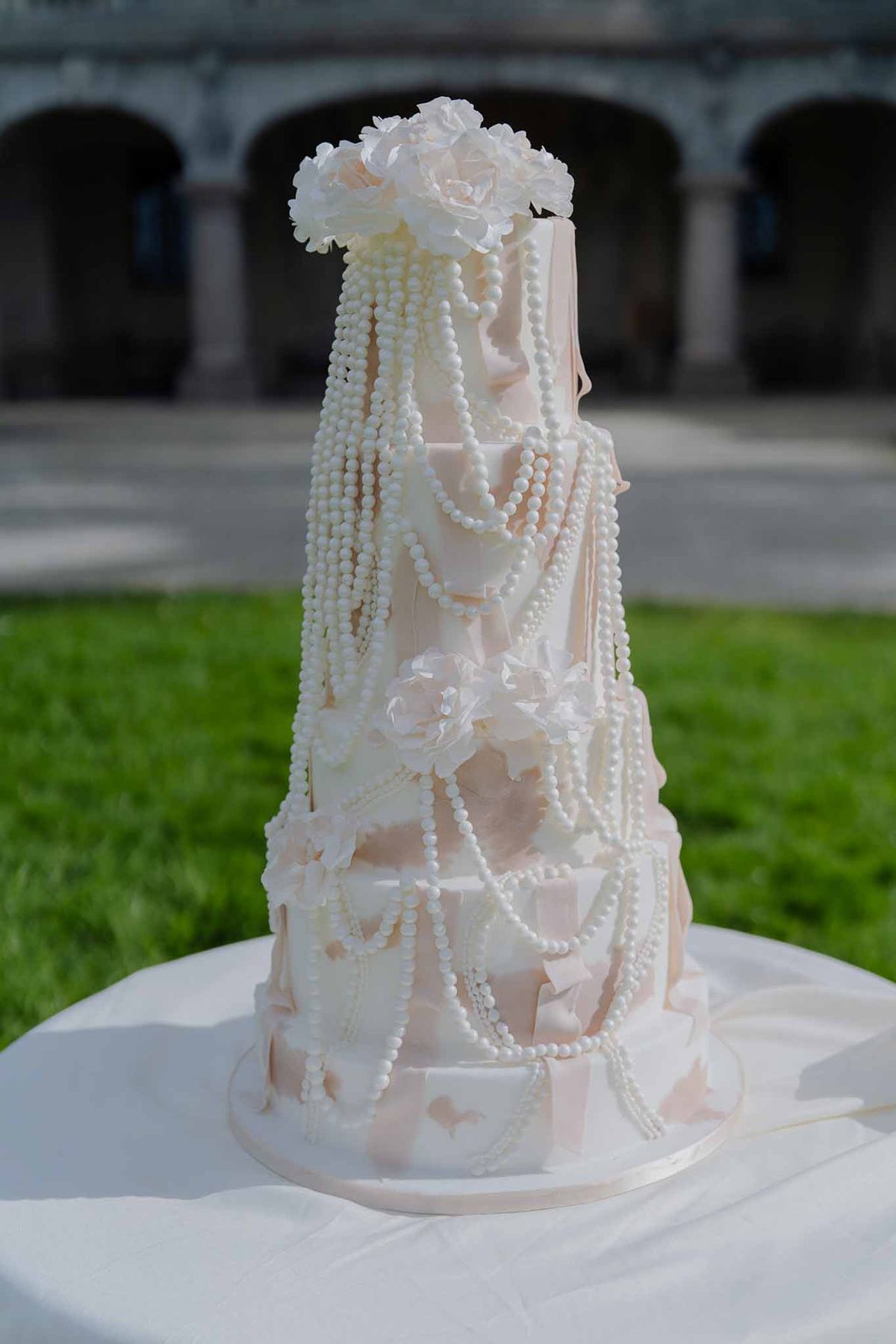 Multi-tier blush pink fondant cake with draped panels cascading sugar pearls and white roses
