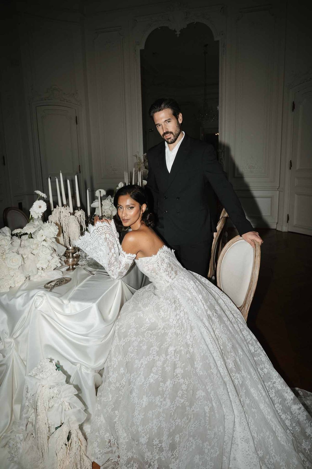 Bride and groom seated at elegantly set reception table in classical indoor venue