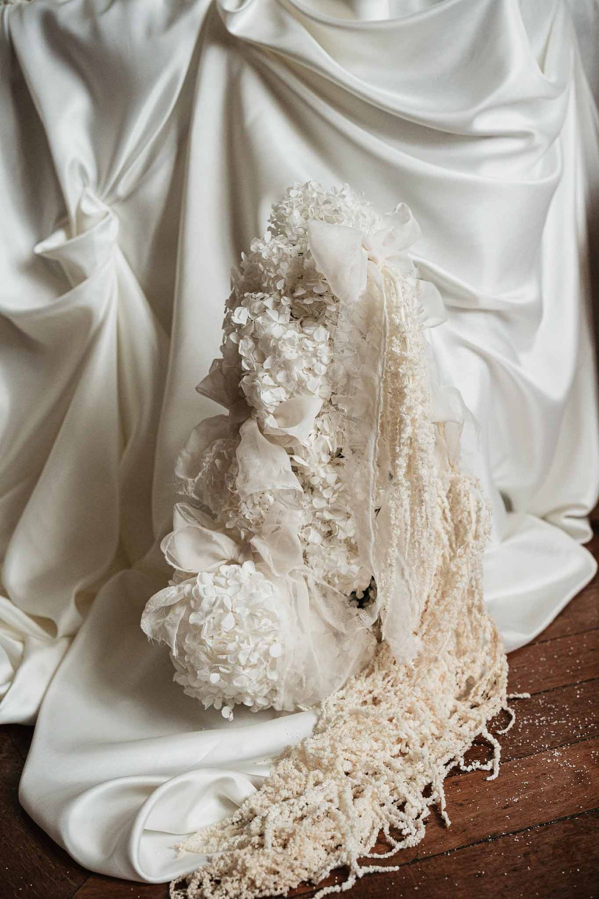 Wedding cake decorated with white hydrangeas and cream peonies with trailing lace veil on dark wood surface