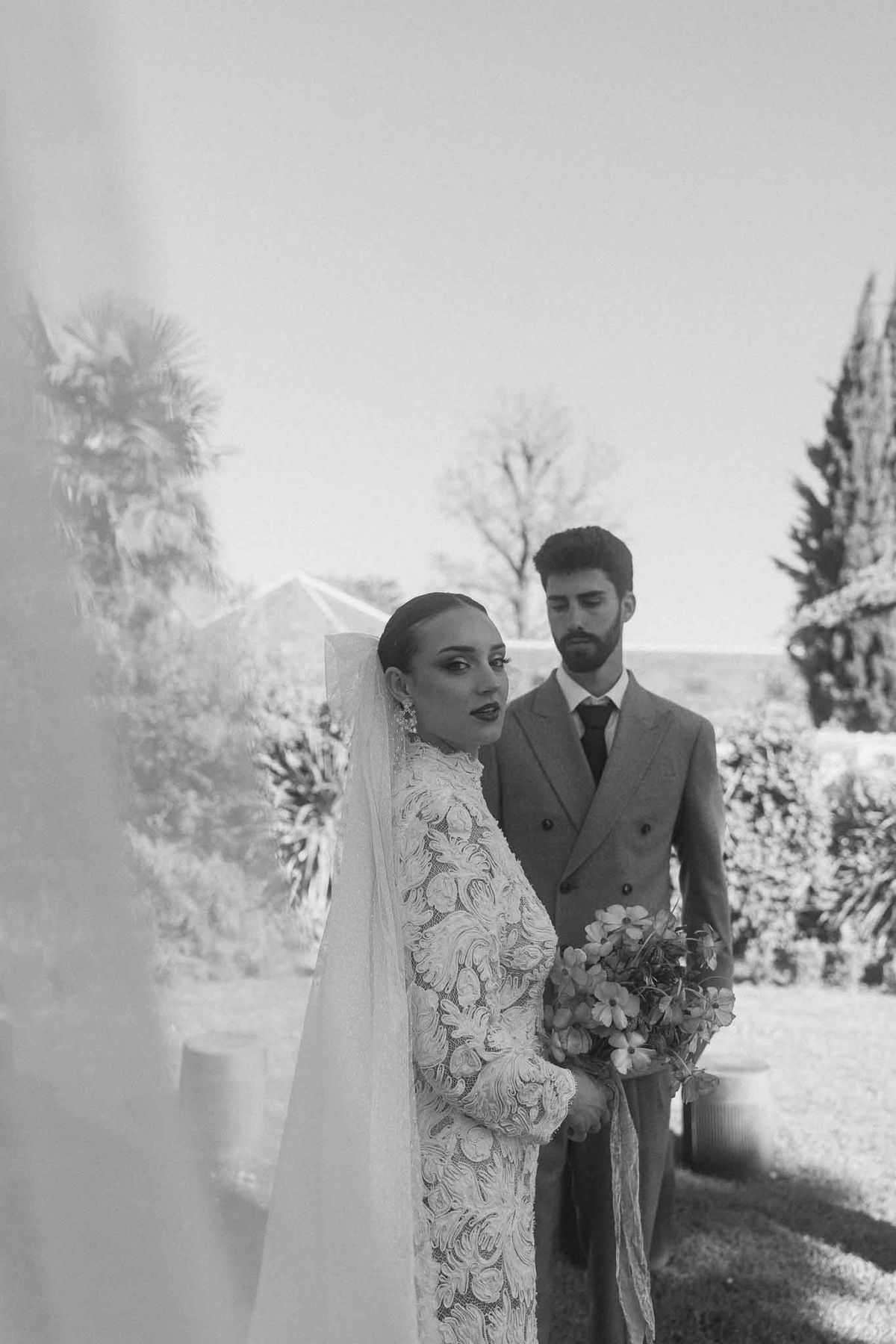Bride and groom walking together down cypress-lined garden pathway at outdoor estate wedding venue