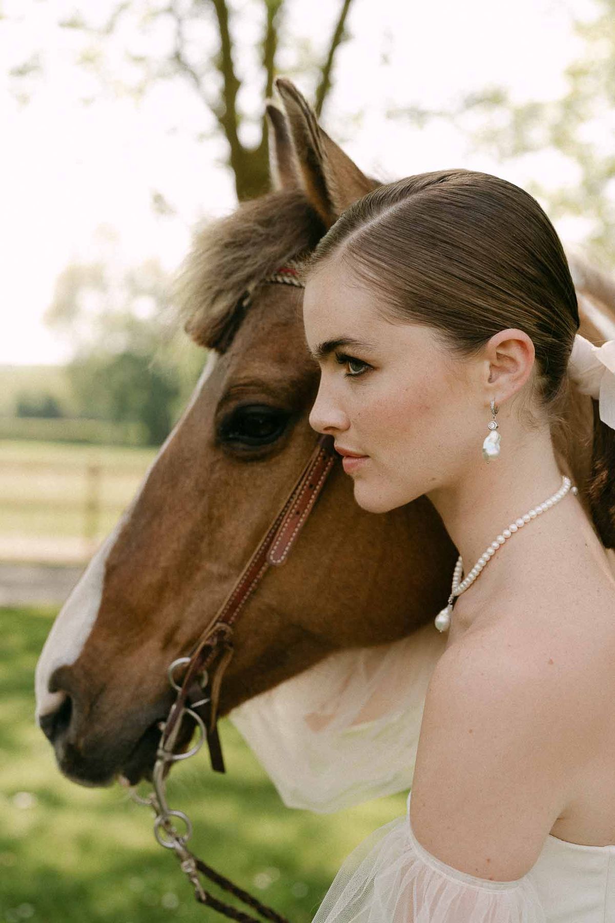 Bride in ivory dress posing with brown horse at countryside equestrian venue