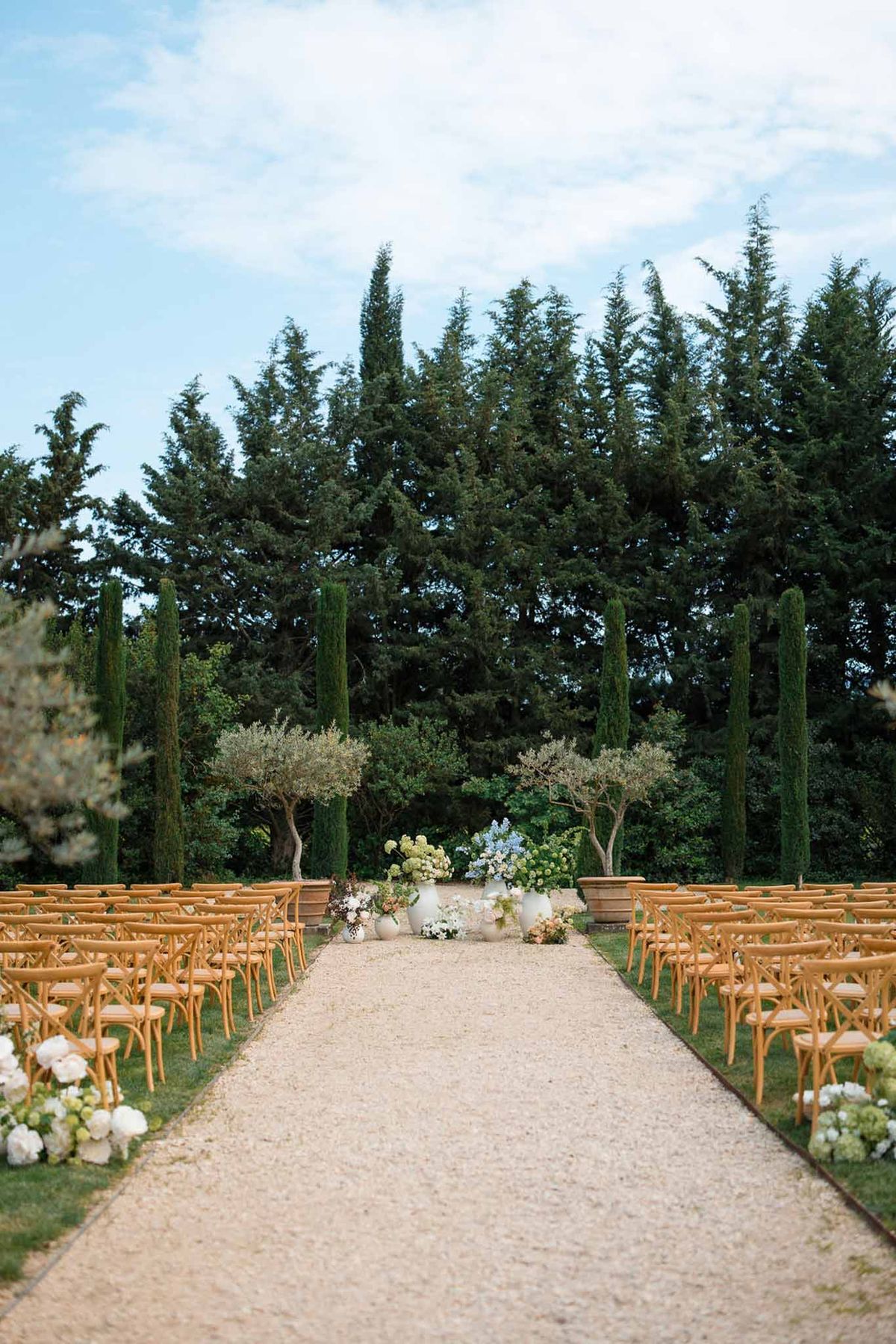 Outdoor wedding ceremony setup with wooden chairs and floral arrangements in Mediterranean garden setting