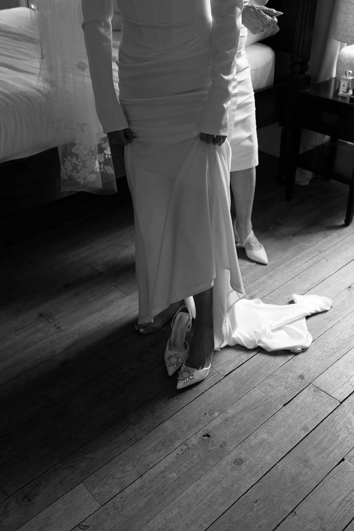 Black and white waist-down shot of bride in ruched gown with crystal slingback heels on wood floor