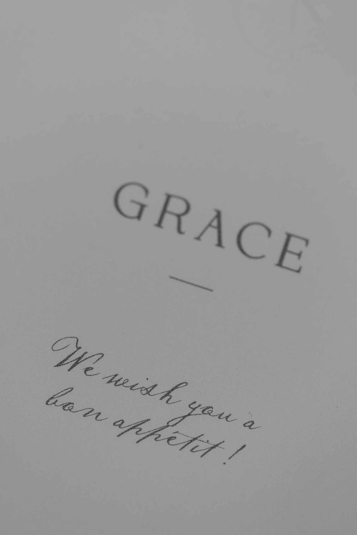 Close-up of a pale grey wedding place card with the name Grace in serif capitals and handwritten bon appetit message