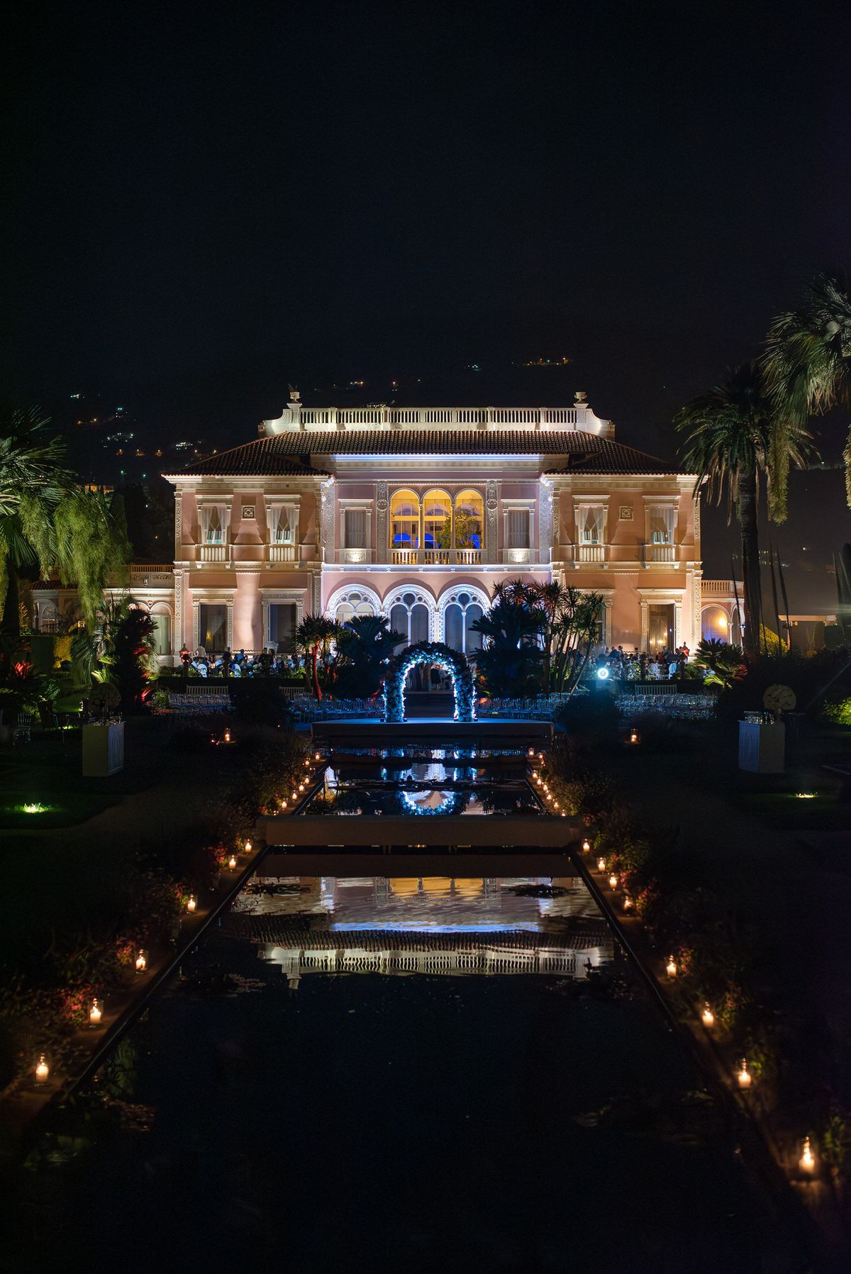 Nighttime wedding ceremony at Belle Epoque villa with floral arch, reflecting pool, and candlelit aisle for 100 guests