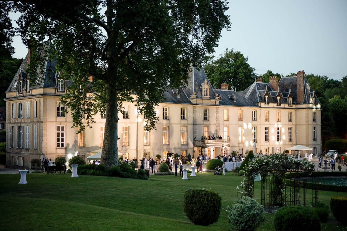 Dusk wide-angle view of cocktail hour on chateau terrace with guests mingling around white cocktail tables