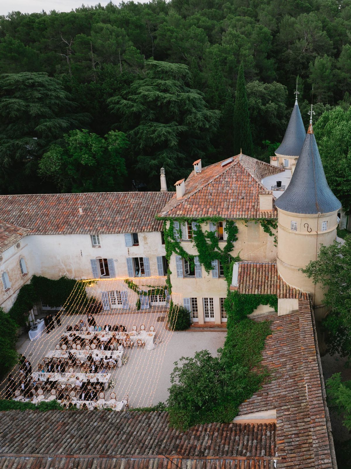 Aerial view of outdoor wedding reception dinner in chateau courtyard with fairy lights and long banquet tables