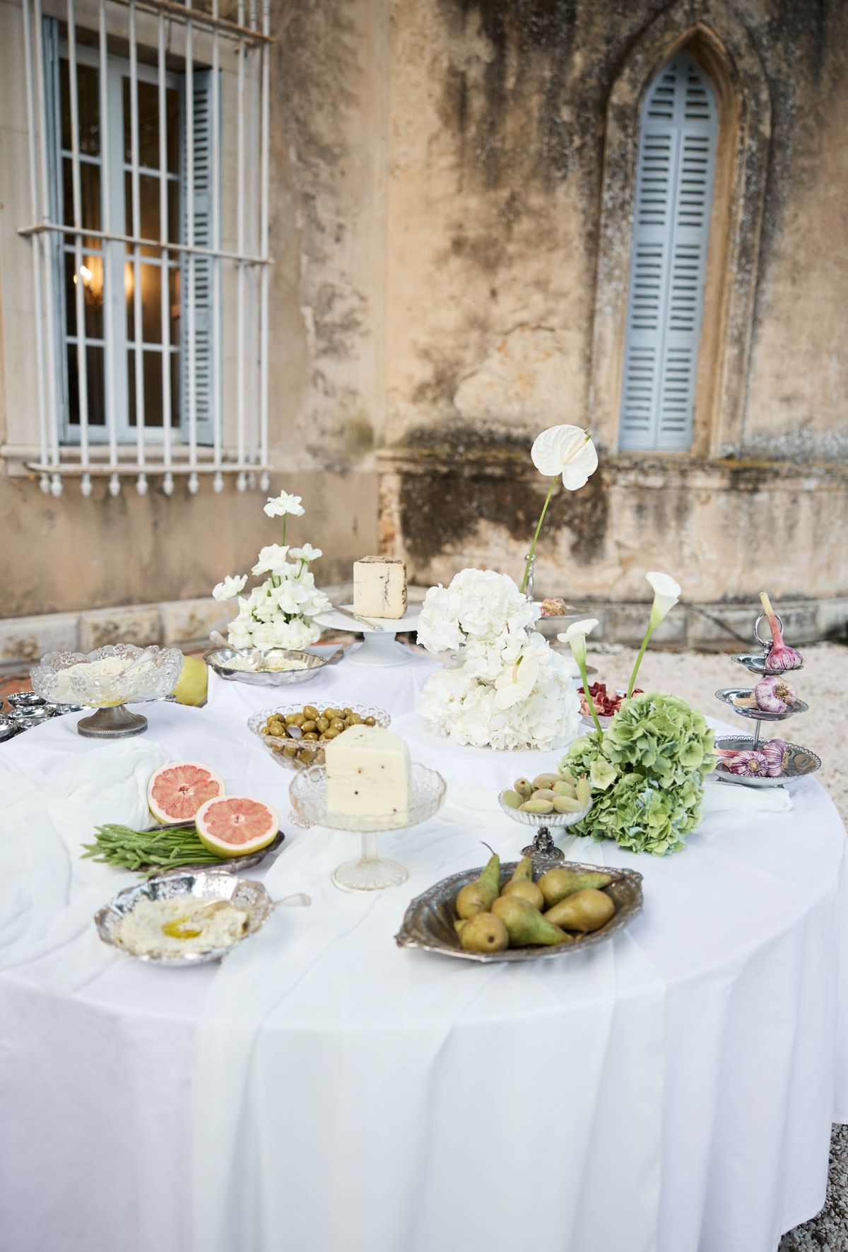 Grazing table with white hydrangeas calla lilies cheeses and fruits before chateau stone facade