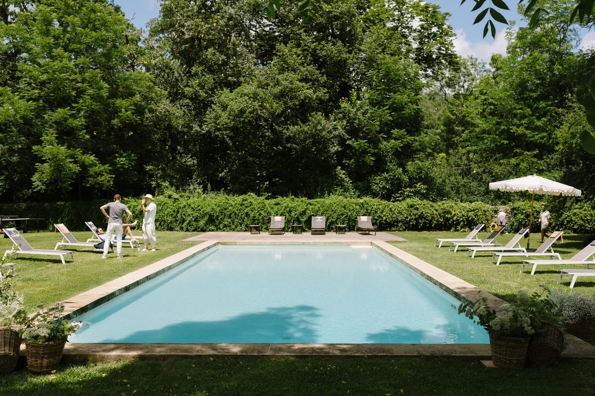 Pool area with guests relaxing around turquoise water, sun loungers, and cream umbrella on venue grounds