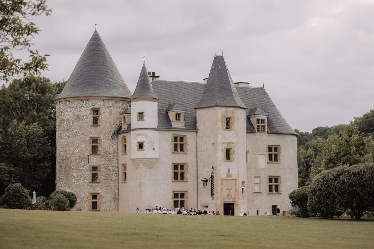 Multi-turreted limestone chateau with slate dormers and 50 guests gathered on front lawn