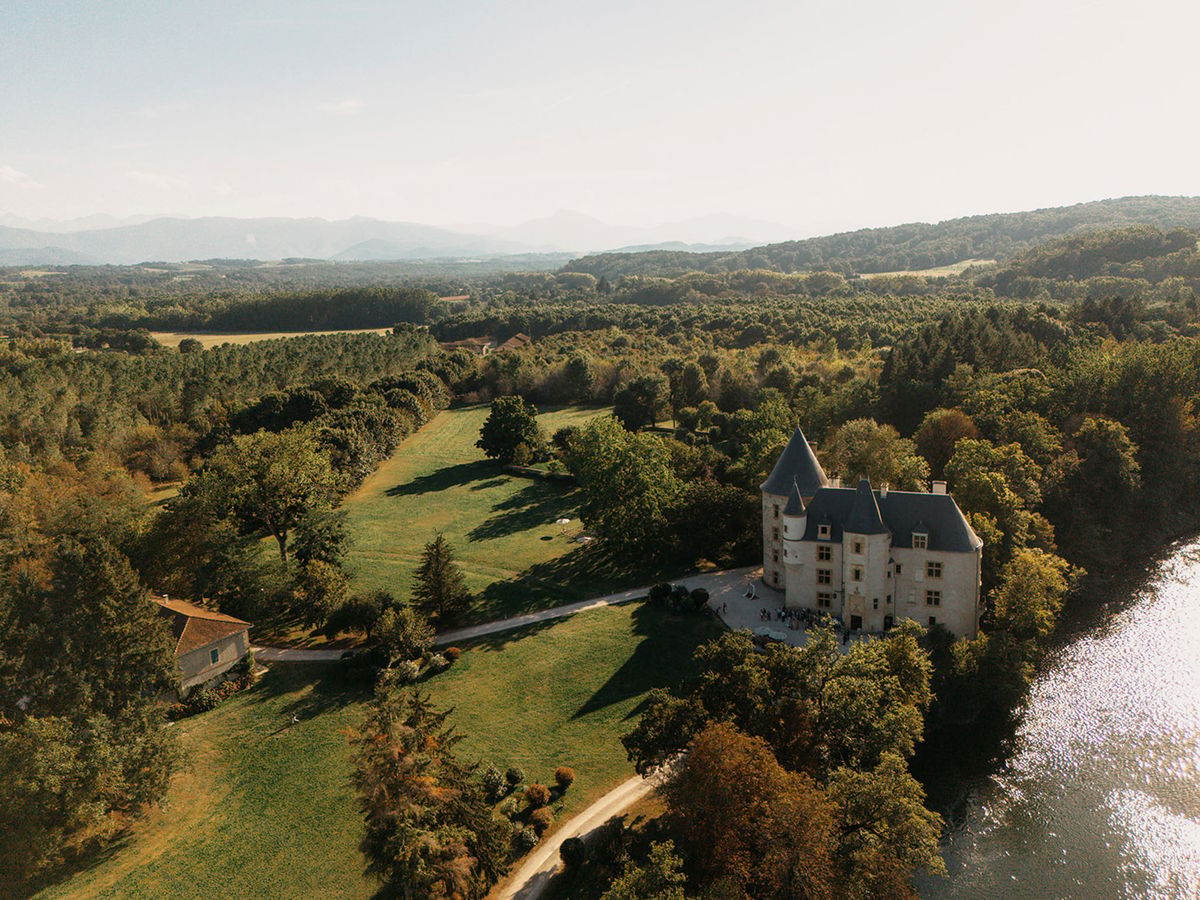 Aerial drone view of a French chateau with towers beside a lake surrounded by autumn woodland and mountains