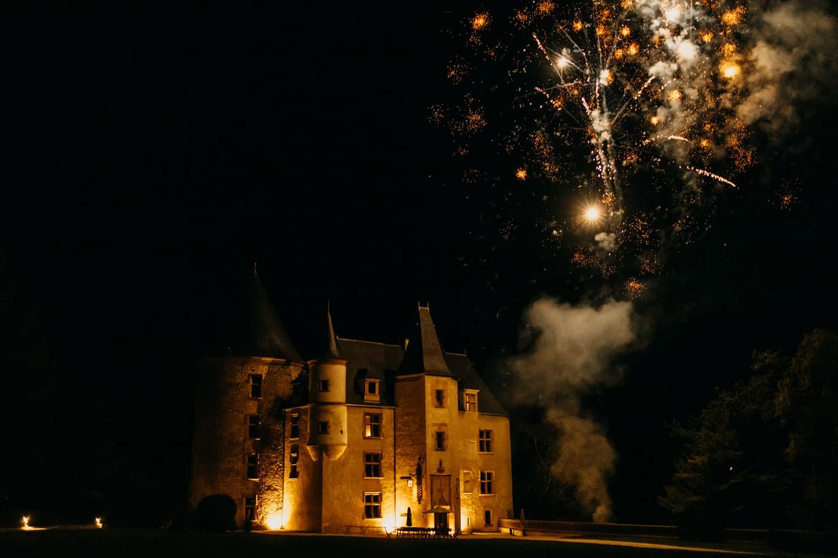 French chateau with turret roofs lit by amber uplighting with fireworks bursting overhead at night