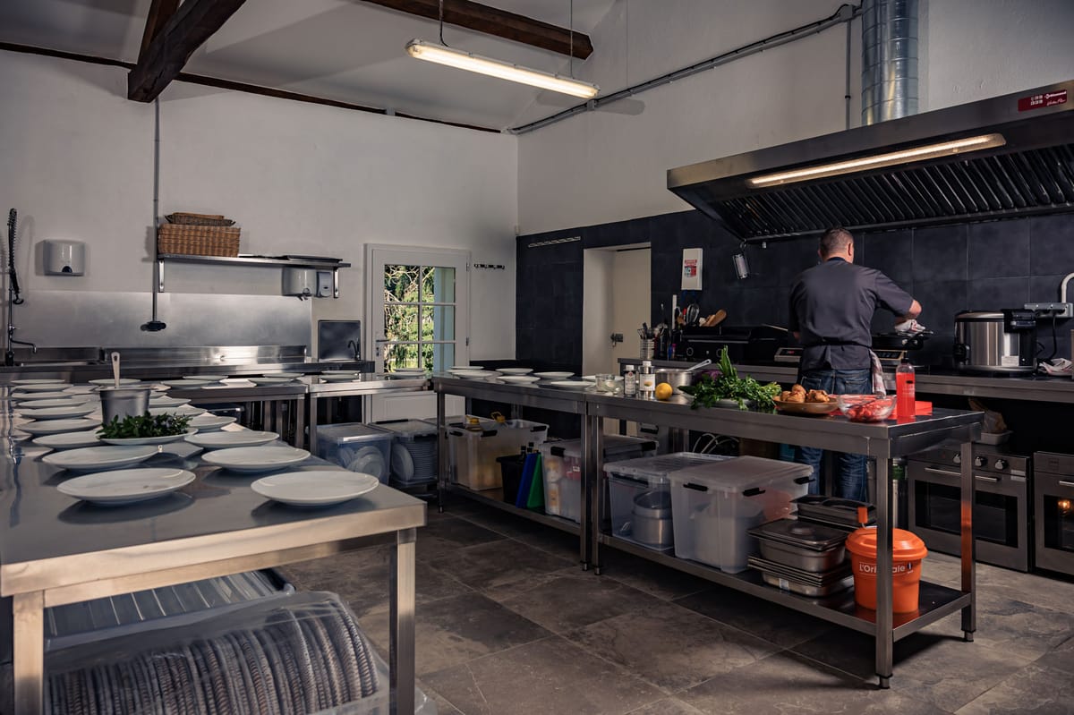 Professional catering kitchen with stainless prep tables plated dishes wooden beams and stone tile floor