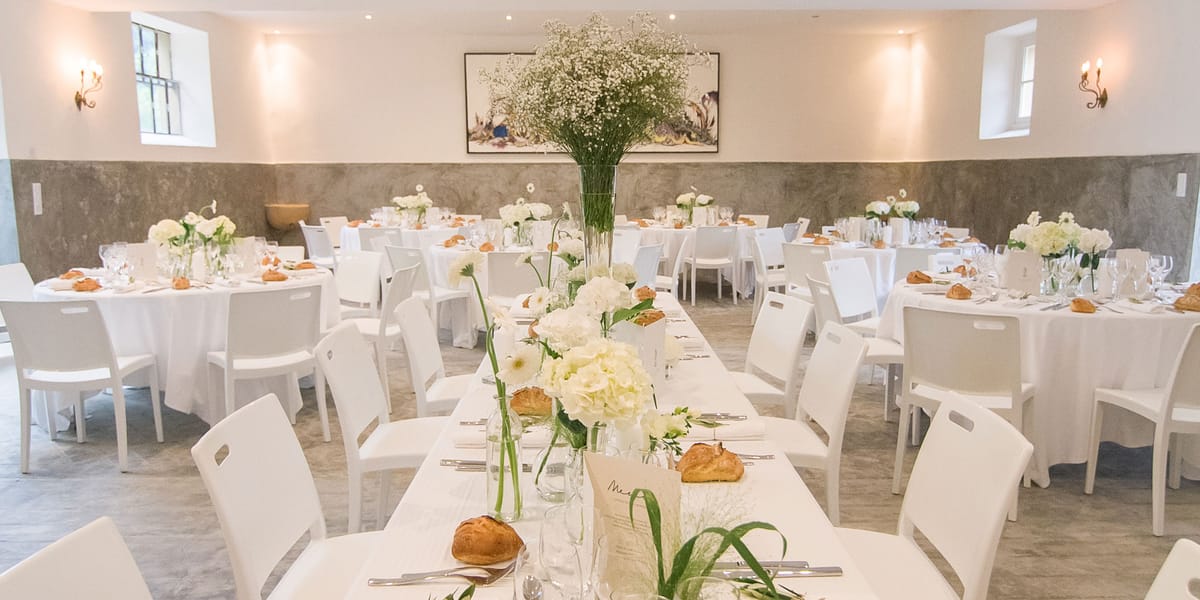 All-white indoor reception room with hydrangea centerpieces, gypsophila statement vase, and modern chairs